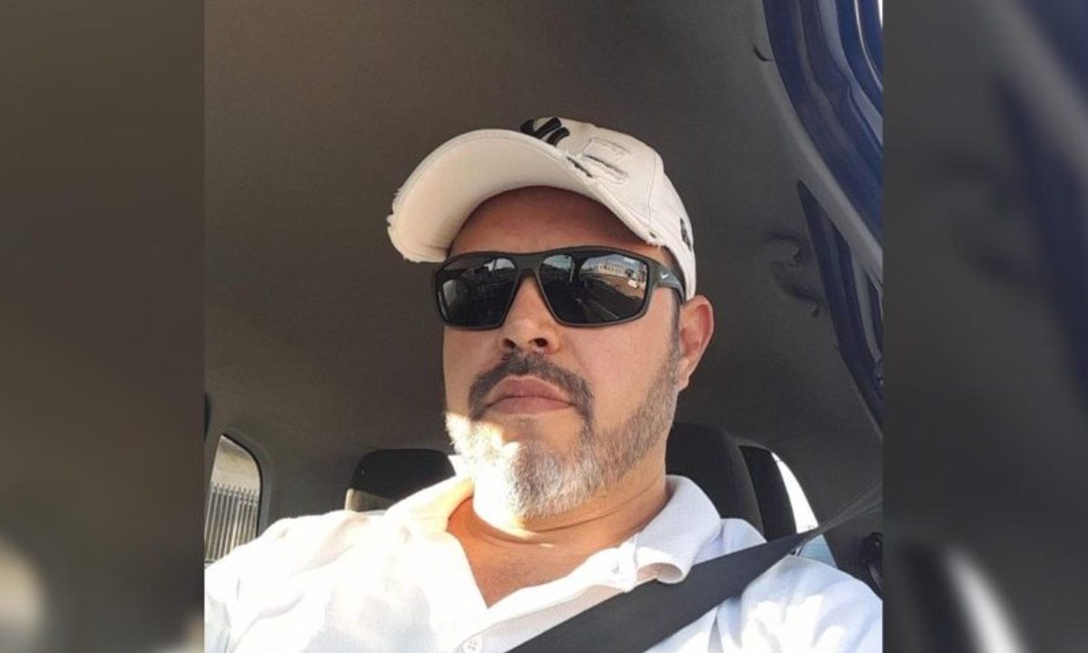 Na foto, motorista que morreu ao ser atropelado por carro na BR-277 aparece sentado dentro de um carro, posando para selfie e usando boné branco, óculos escuros e camisa branca. O homem tem barba grisalha e pele branca.