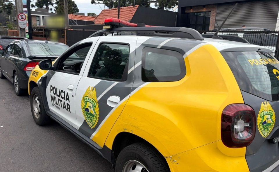 Foto mostra viatura da Polícia Militar estacionada próximo ao cruzamento onde motorista de veículo Corsa passou por cima de motociclista após supostamente furar sinal vermelho no bairro Alto Boqueirão, em Curitiba.