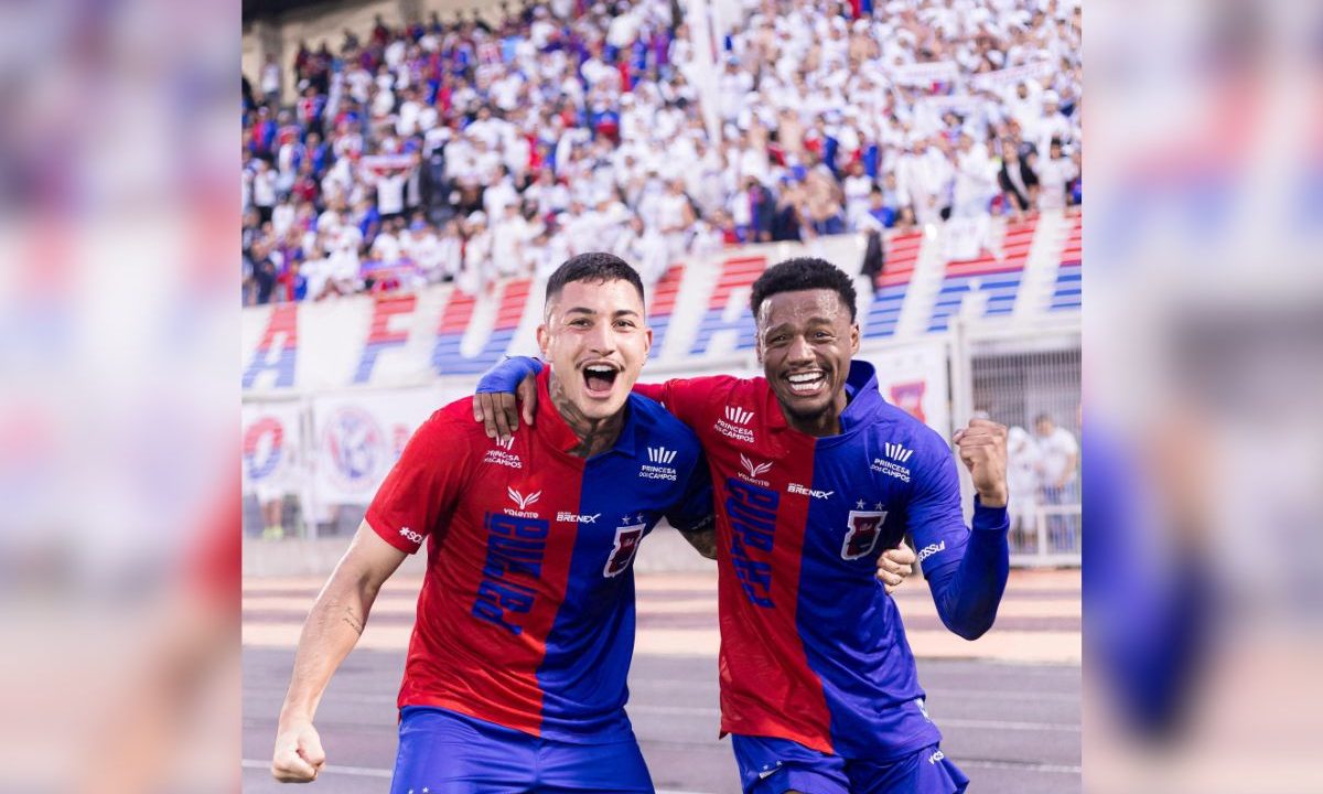 Dois jogadores do Paraná Clube comemoram abraçados após a vitória sobre o Araucária no Gigante do Itiberê. Ao fundo, a torcida tricolor aparece nas arquibancadas celebrando o resultado da semifinal da Segundona Paranaense.