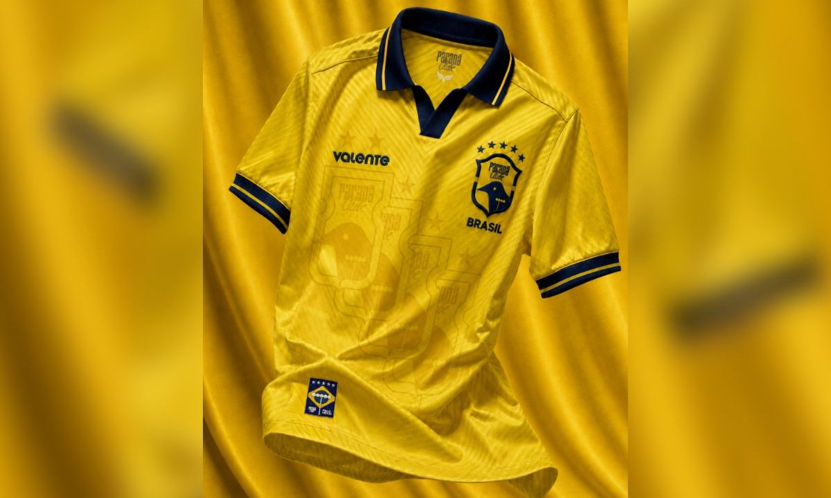 Imagem mostra a camisa do Paraná Clube 2026 em fundo amarelo, inspirada no uniforme da Seleção Brasileira campeã do mundo em 1994. A peça tem predominância da cor amarela, detalhes em azul na gola e mangas, escudo estilizado do clube e referências visuais ao tetra mundial
