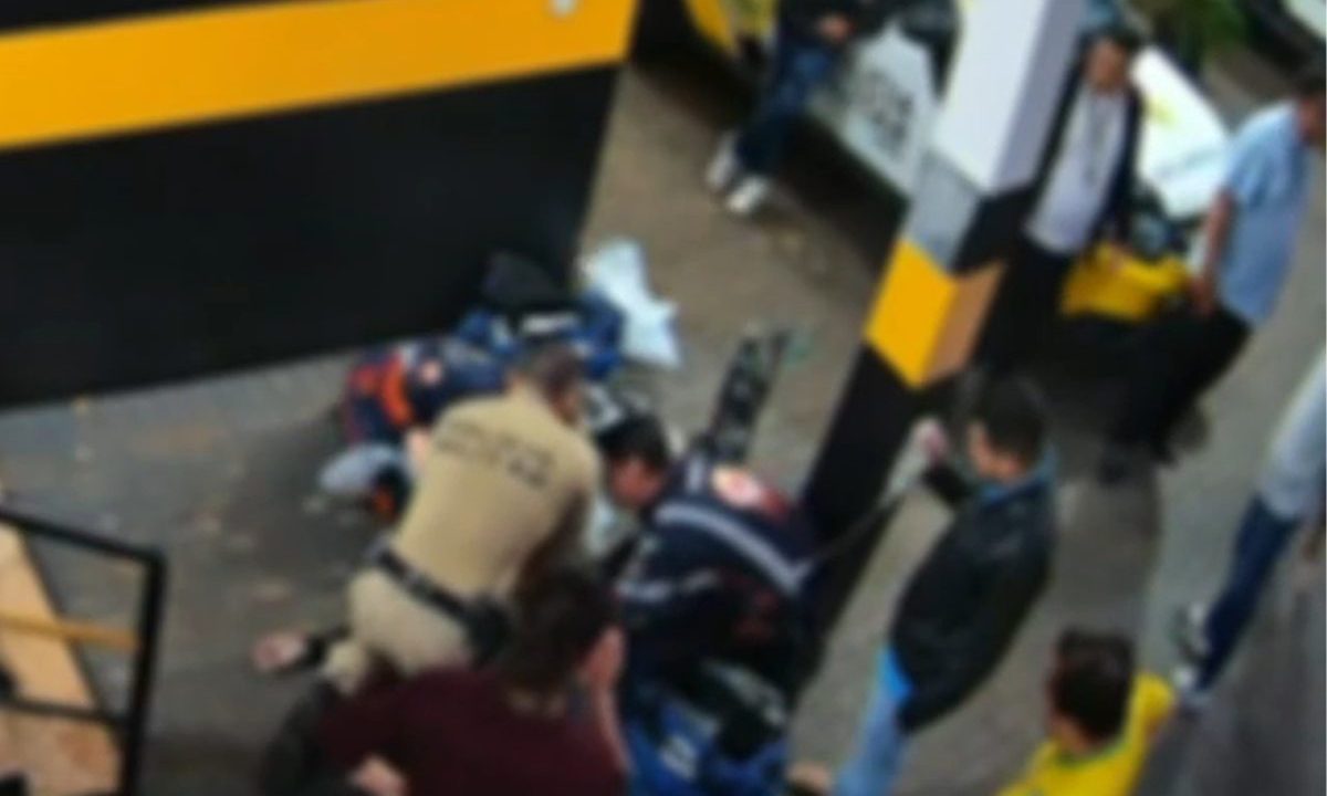 Imagem mostra um policial e um socorrista do Samu reanimando uma passageira em um posto da Polícia Rodoviária Estadual. A mulher foi reanimada após 40 minutos de massagem cardíaca. O policial e o socorrista estão agachados em torno da mulher. Outras pessoas estão ao redor olhando a situação.