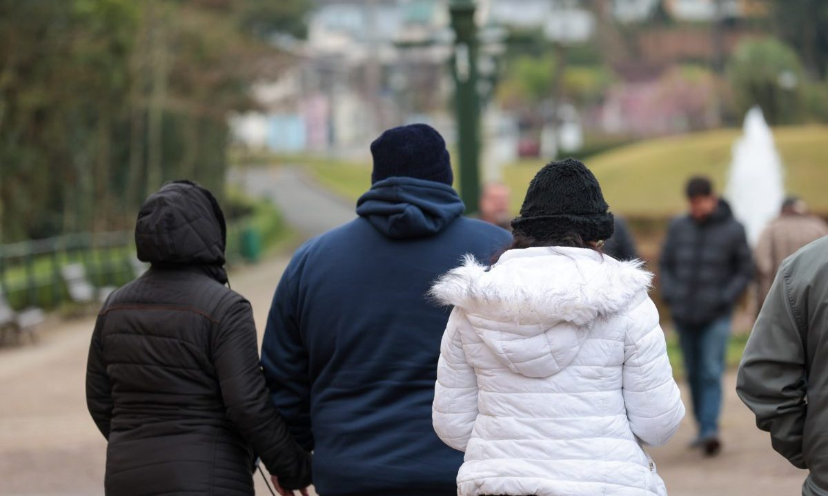 Imagem ilustrativa para a previsão do tempo nesta quinta-feira em Curitiba. Imagem mostra três pessoas com blusa de frio. Elas estão de costas. Uma mulher usa blusa preta. O homem, no meio, usa blusa azul marinho. E a outra mulher veste blusa branca.