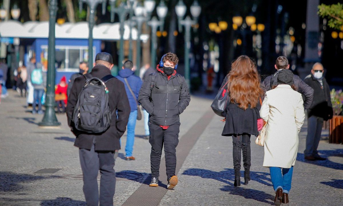Imagem ilustrativa para a previsão do tempo em Curitiba neste sábado. Foto mostra diversas pessoas agasalhadas andando em uma praça na capital.