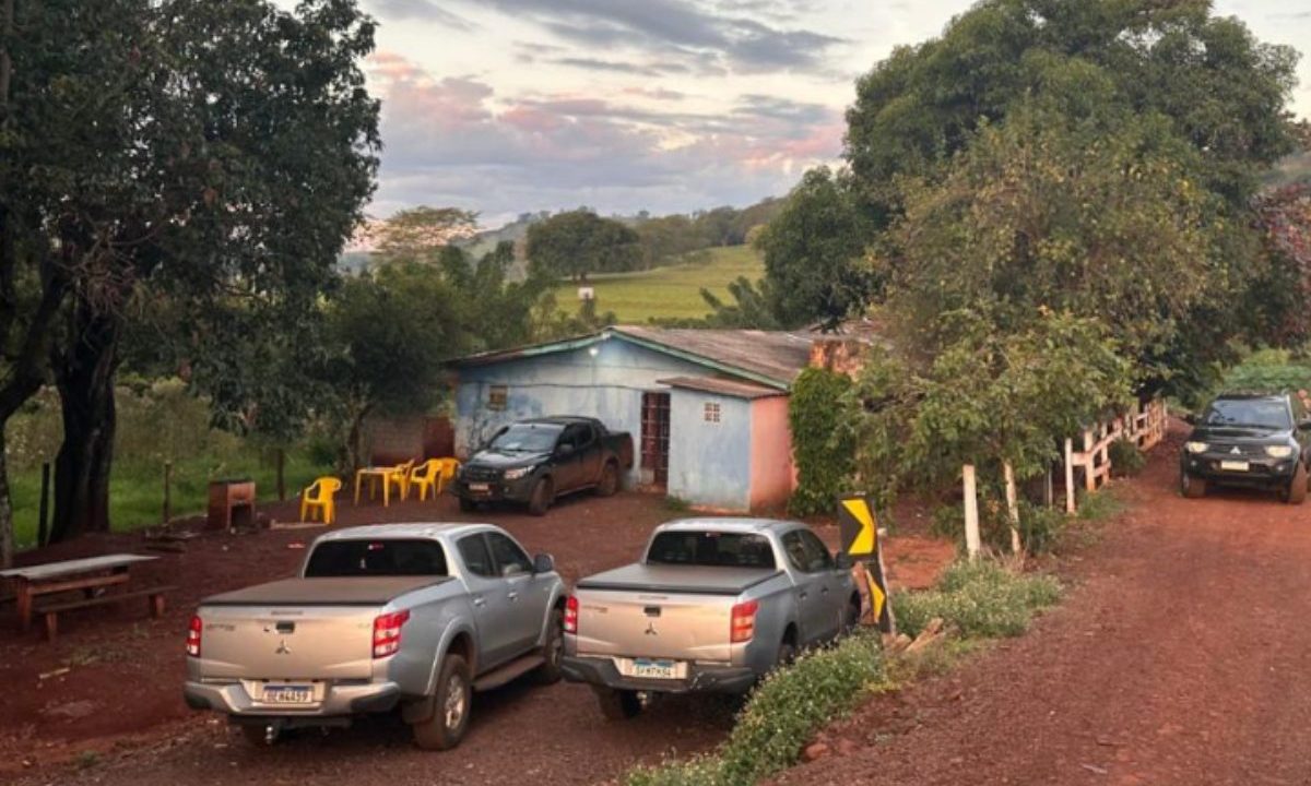 Na imagem aparece a entrada do prostíbulo, uma pequena casa, na cor azul, de telha, suspeito de manter paraguaias regime de escravidão sexual. Na frente do local, alguns carros, cadeiras, bancos e bastante vegetação. No céu algumas nuvens.