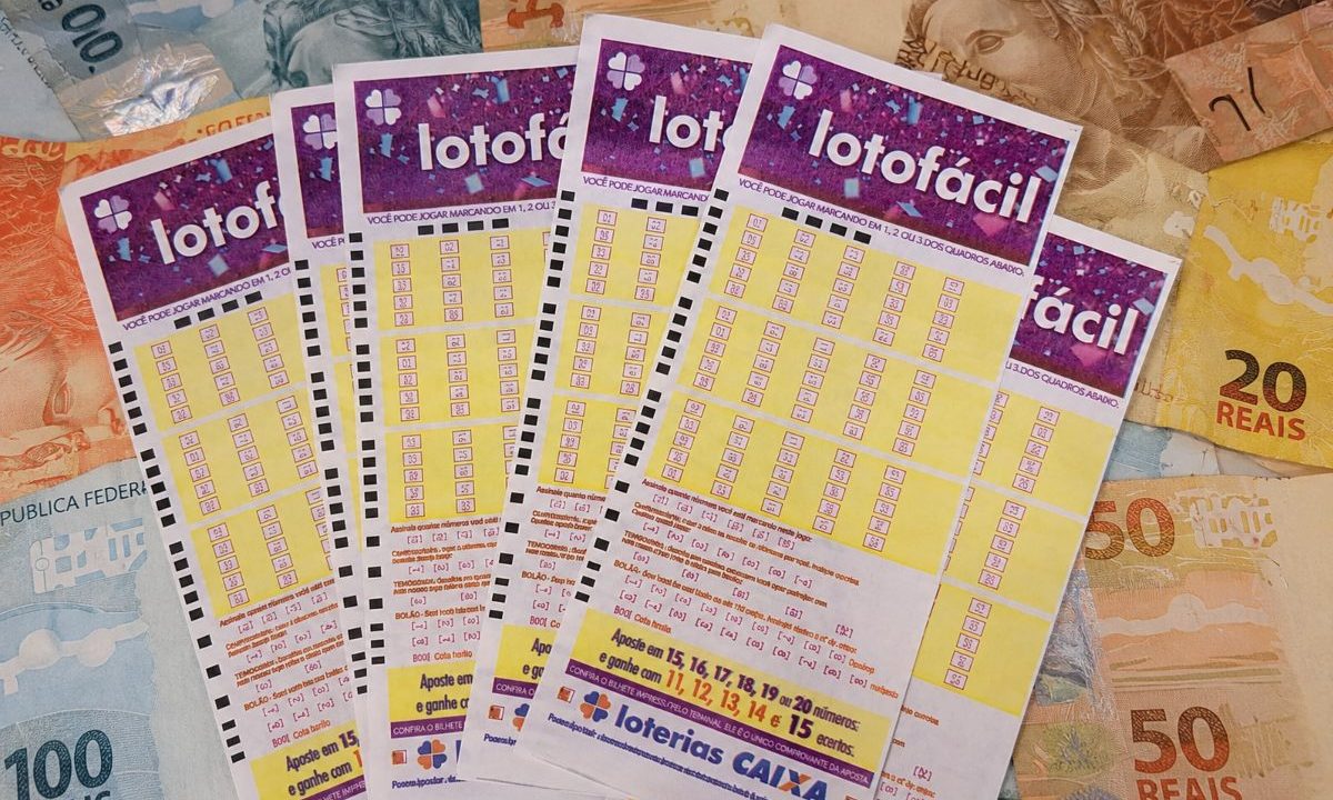 Volantes da Lotofácil 3694 em cima de notas de dinheiro