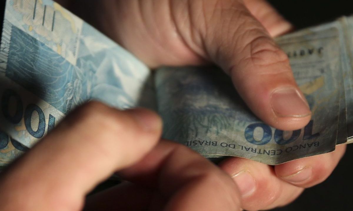 Mão manuseando notas de R$ 100, representando o resultado da Lotofácil 3688 de hoje, que está com prêmio milionário.