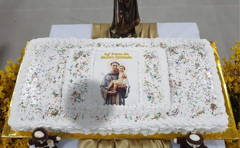 Grande bolo decorado com glacê branco e imagem do padroeiro para a festa de Santo Antônio em Cascavel.