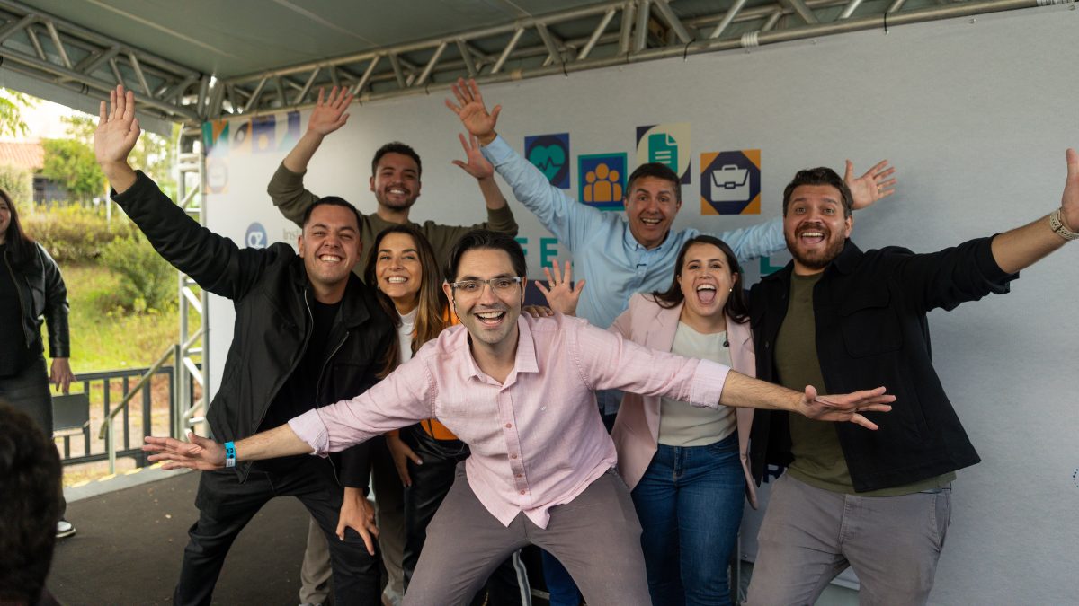 Grupo de sete apresentadores e jornalistas da RIC Record sorrindo e acenando com os braços abertos no palco do Festival RIC Record.