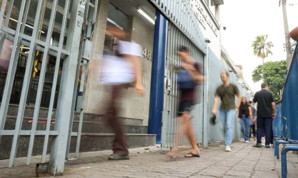Fotografia com efeito de desfoque de movimento mostrando jovens passando apressados por um portão de grades de metal de um prédio. Imagem ilustrativa para matéria: Inscrições do Enem 2026 se encerram nesta sexta-feira