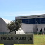 Fachada do prédio do Superior Tribunal de Justiça (STJ) em Brasília, com gramado em primeiro plano e placa de identificação, ilustrando matéria sobre o processo de assédio sexual envolvendo ministro.