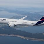 Avião comercial branco da LATAM Airlines voando em altitude de cruzeiro sobre uma faixa de litoral e ilhas, ilustrando a expansão da oferta de norte do paraná voos.