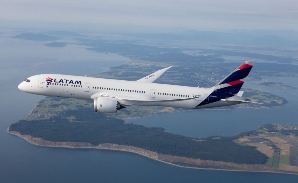 Avião comercial branco da LATAM Airlines voando em altitude de cruzeiro sobre uma faixa de litoral e ilhas, ilustrando a expansão da oferta de norte do paraná voos.