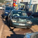 Carro Volkswagen Golf de cor escura com a parte frontal completamente amassada e airbags acionados, parado na lateral de uma via urbana com agentes de trânsito ao fundo, ilustrando a cena onde o motorista detido foi interceptado.