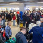 Vista interna do saguão de embarque lotado de passageiros com malas em filas de check-in, destacando pessoas de costas e de perfil esperando atendimento no Aeroporto de Assunção durante o fluxo da Copa do Mundo.