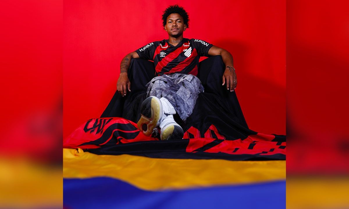 Jorge Rivaldo sentado sobre bandeira da Colômbia durante ensaio de apresentação como novo jogador do Athletico.