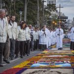 Fiéis participam da procissão de Corpus Christi em Curitiba, caminhando ao lado dos tradicionais tapetes coloridos confeccionados nas ruas da cidade.