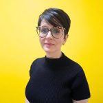 Silvia Oliveira, editora da Banda B, em frente a uma parede amarela