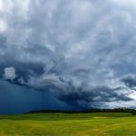 Nuvens densas e escuras de tempestade avançam sobre área de campo aberto, indicando mudança brusca no tempo e possibilidade de chuva intensa.