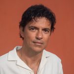 Foto do cantor Jorge Vercillo, de camisa branca e diante de uma parede laranja. Ele traz show para Curitiba.