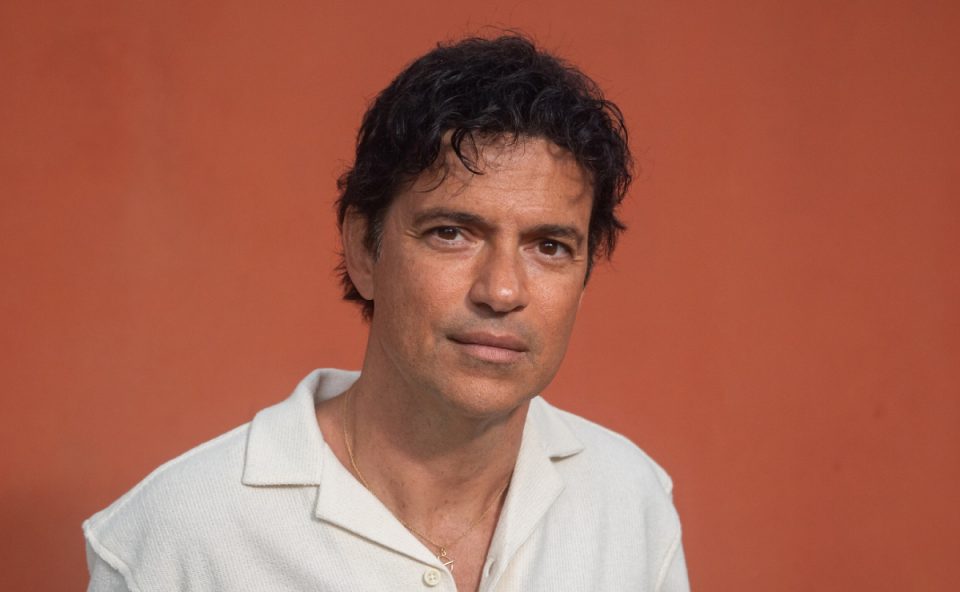 Foto do cantor Jorge Vercillo, de camisa branca e diante de uma parede laranja. Ele traz show para Curitiba.