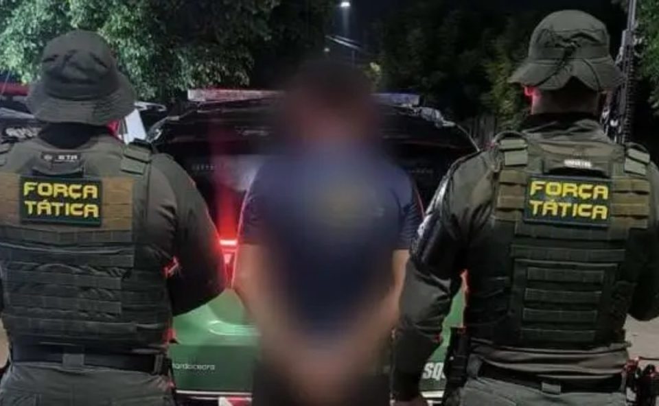 Pai é preso por colocar fogo em casa da ex-companheira no interior do Ceará. Foto mostra o suspeito no meio de dois policiais.