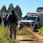 Viatura da Polícia Científica e equipes de segurança atendem ocorrência em uma estrada rural cercada por vegetação em Ponta Grossa, onde um motociclista foi encontrado morto.