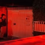 Foto mostra policial militar entrando na casa onde homem atirou contra a companheira e tirou a própria vida em seguida, em Pinhais. Viatura está com o giroflex ligado em frente ao imóvel