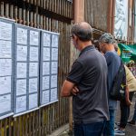 na imagem, pessoas em frente ao painel com vagas de emprego que vão ser ofertadas no mutirão da evangelizar nesta quinta-feira (11)