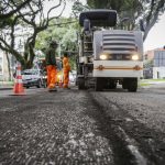 Equipe realiza obras de recuperação do asfalto em uma via de Curitiba com máquinas e trabalhadores atuando na pista.