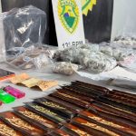 Foto mostra mesa com drogas apreendidas com olheiro no Parolin. Na mesa há isqueiros coloridos, sedas e pequenas embalagens com maconha e cocaína. Tudo está alinhado sobre a mesa