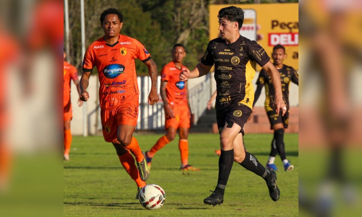 Atleta do FC Cascavel conduz a bola em partida da Série D enquanto é marcado por jogador adversário durante confronto da competição nacional.