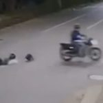 Imagem de câmera de segurança mostra uma mulher caída no meio de um cruzamento durante a noite. A vítima aparece sobre a pista poucos segundos antes de ser atropelada por um carro. A cena ocorreu em uma avenida movimentada e registra os momentos que antecederam o acidente.