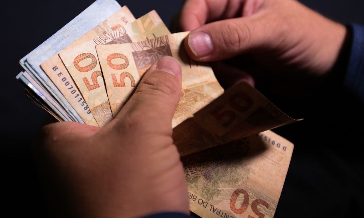 Mão contando notas de dinheiro, simbolizando o prêmio da Loteria Federal 6072.