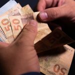 Mão contando notas de dinheiro, simbolizando o prêmio da Loteria Federal 6072.