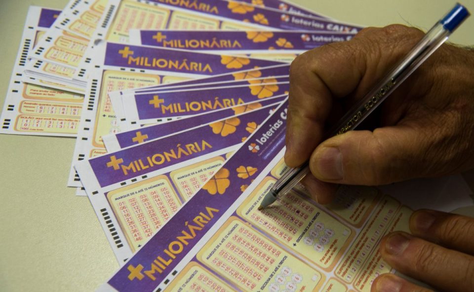 Mão segurando caneta e selecionando dezenas da +Milionária 362.