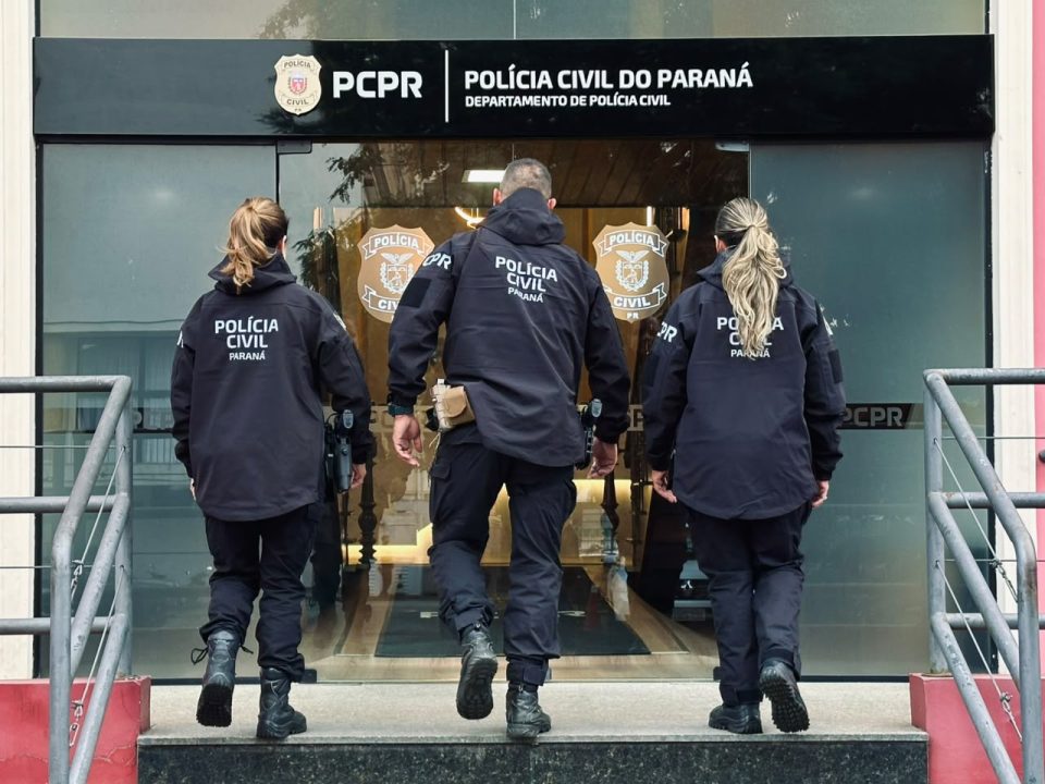 foto mostra o arsenal apreendido em piraquara. suspeito foi preso. foto mostra armas em cima de uma mesa. foto mostra três policiais civis de costas.