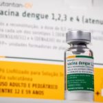 Frasco da vacina contra a dengue desenvolvida pelo Instituto Butantan em primeiro plano, com a embalagem do imunizante desfocada ao fundo.